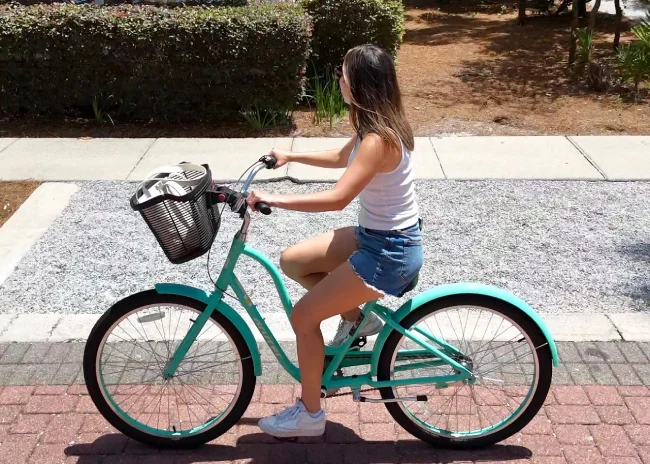 Rider on a teal beach cruiser with a front basket, on a brick bike path lined with hedges