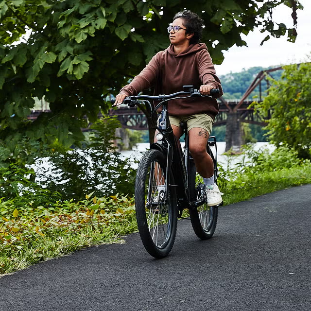 A rider on a low-frame comfort electric bike on a riverside bike path