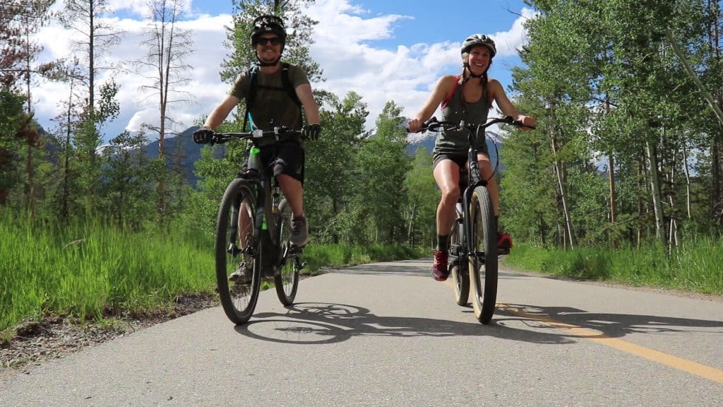 Two riders in helmets on mountain-style electric bikes on a paved trail through the trees